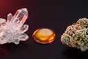Clear THCa crystals, a glossy amber drop of oil and a frosty cannabis bud lined up on a black surface under red rim light.